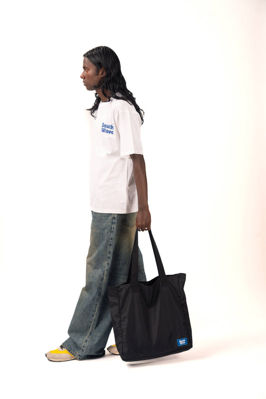 A person wearing a white t-shirt and blue jeans, carrying a black bag with a blue logo.